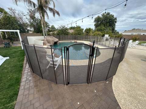 Brown mesh pool fence with arched gate around a lagoon-style pool